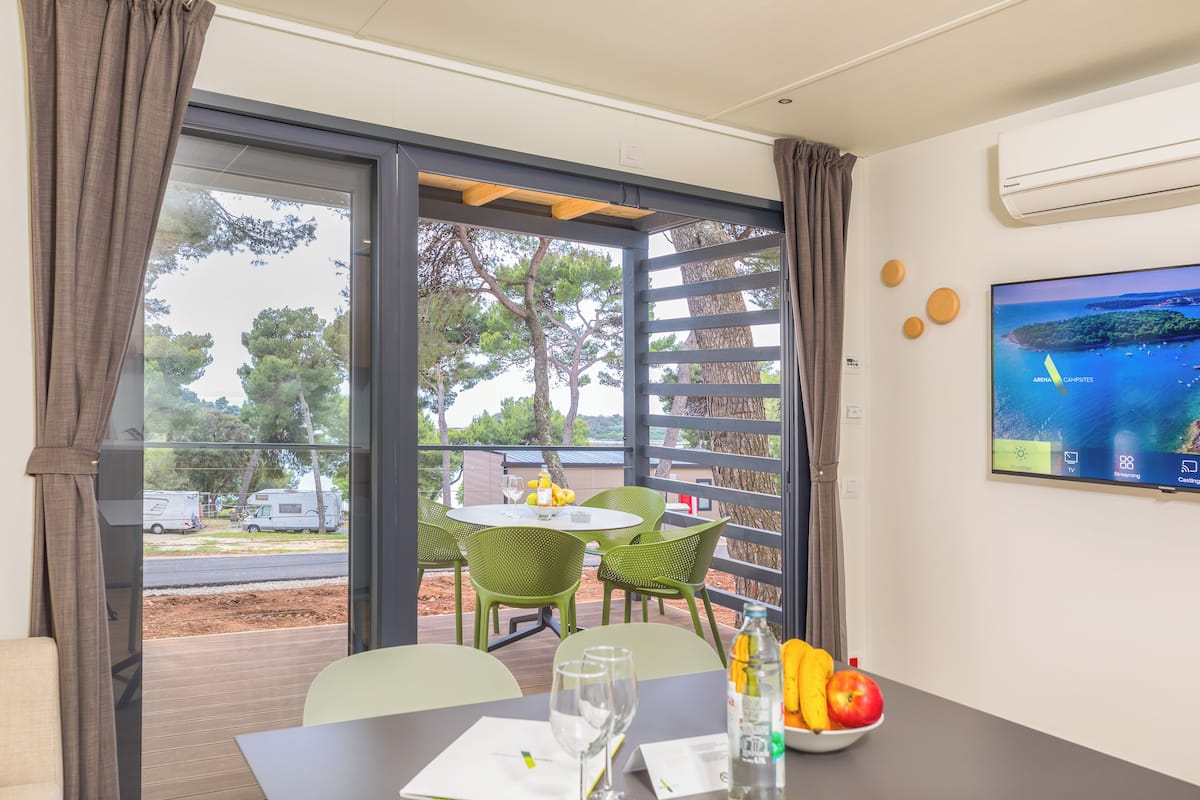 A room with a table set for dining, a TV on the wall, and a view of the outdoors.