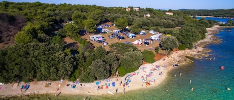 An aerial view of a coastal area with a beach, clear water, and a campsite with tents.