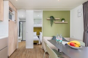 A compact hotel room with a kitchenette, a dining area with a table and chairs, a sofa, a bed, and a bathroom with a shower and toilet.