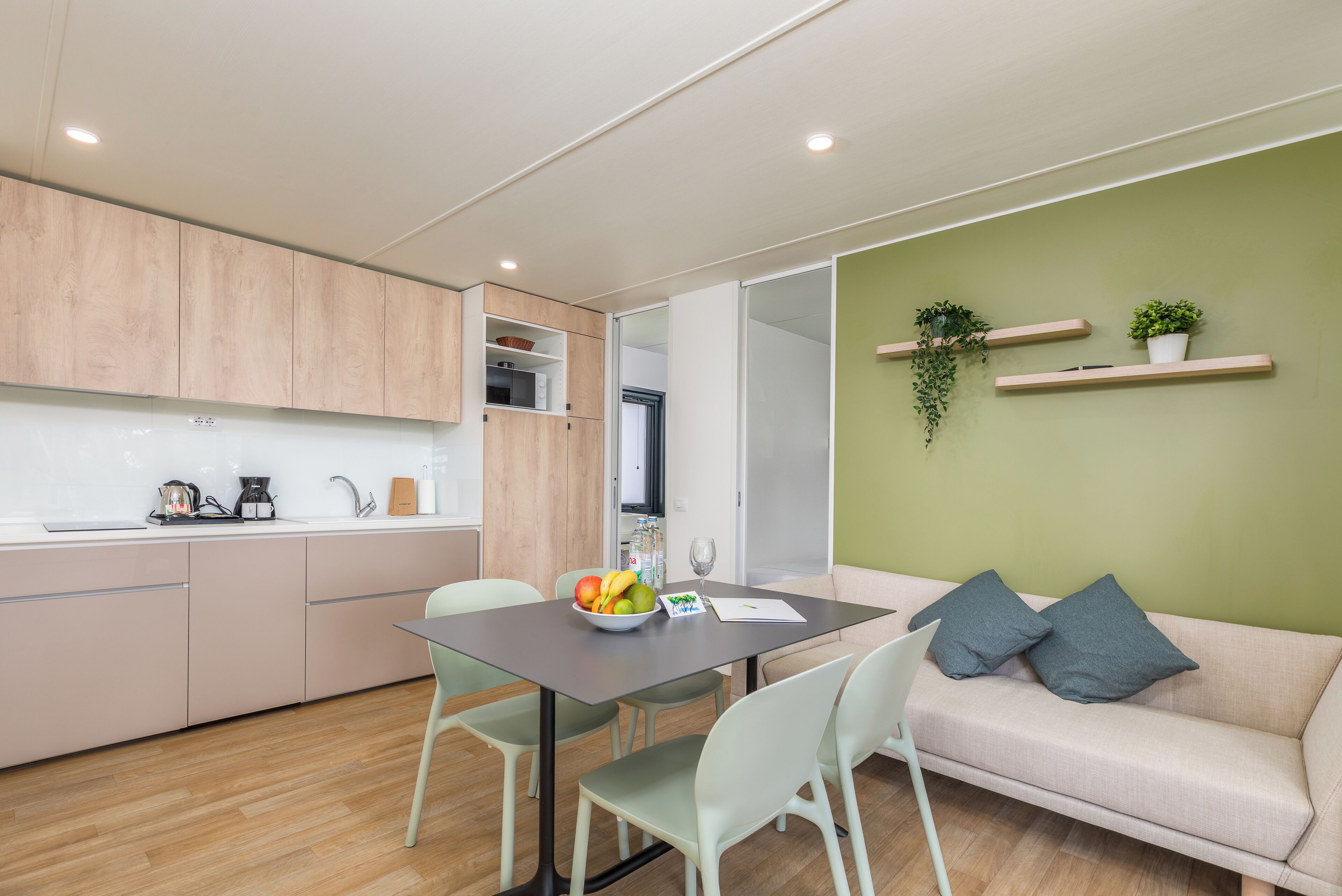 A modern kitchen with a dining area, a sofa, and a green accent wall.