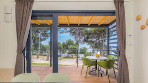 A room with a view of a beach and trees, a table with chairs, and a wooden ceiling. - Arena Indije Mobile Homes (Medulin)