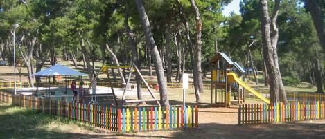 A park with playground equipment, picnic tables, and a fenced area.