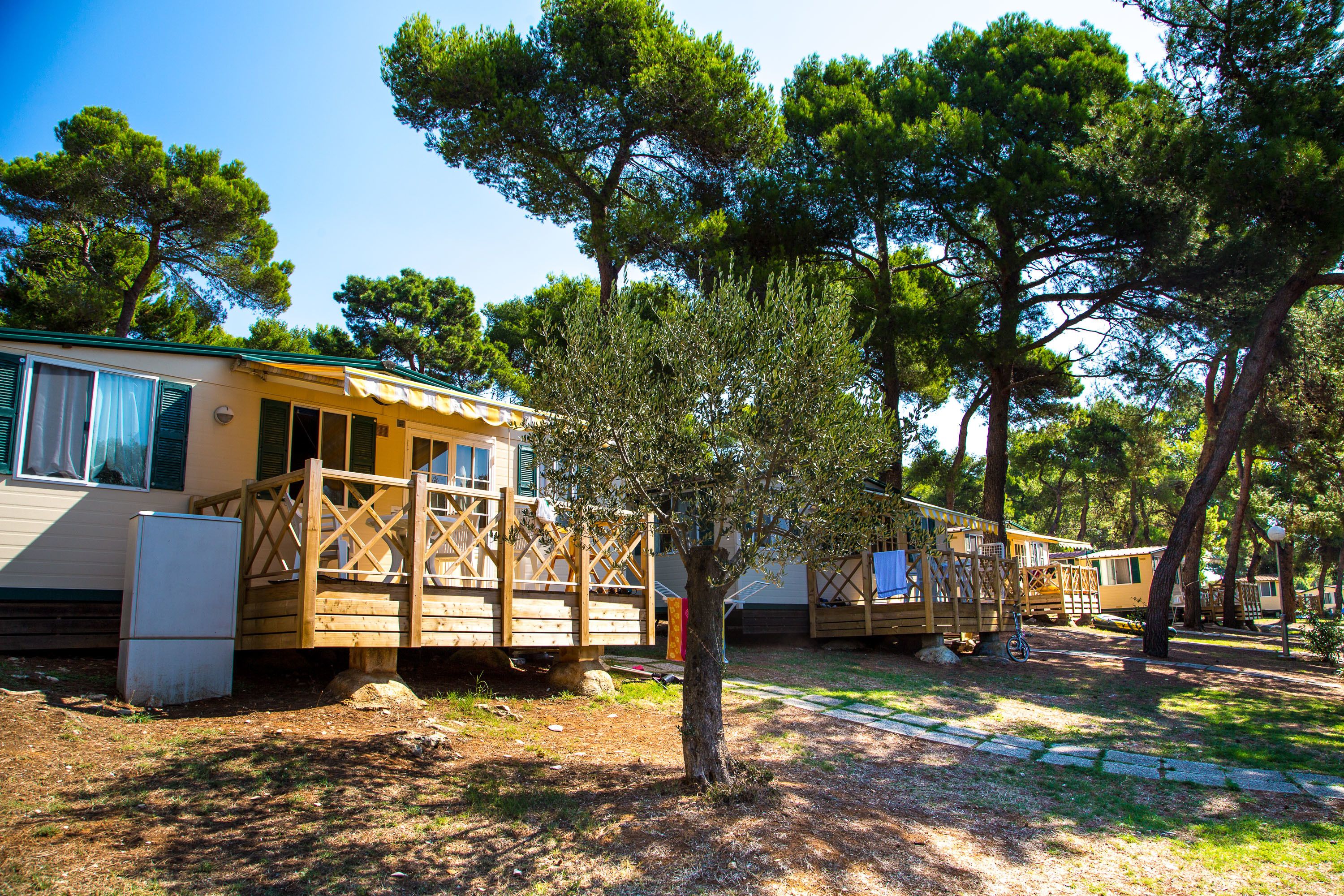 A row of mobile homes with wooden decks and a small refrigerator outside each unit.