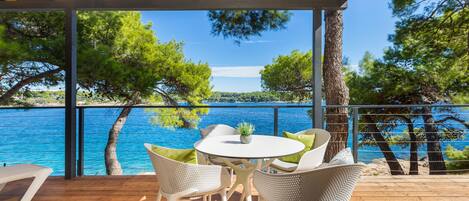 A wooden deck with a table and chairs overlooking a clear blue sea and green trees.