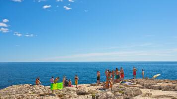 A rocky beach with people sunbathing and swimming in the ocean.