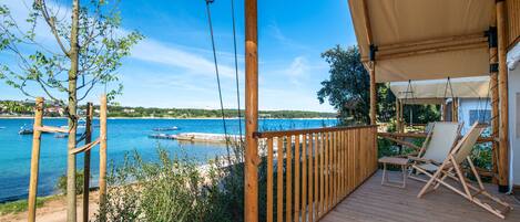 Une terrasse en bois avec vue sur la mer, une chaise et un auvent.