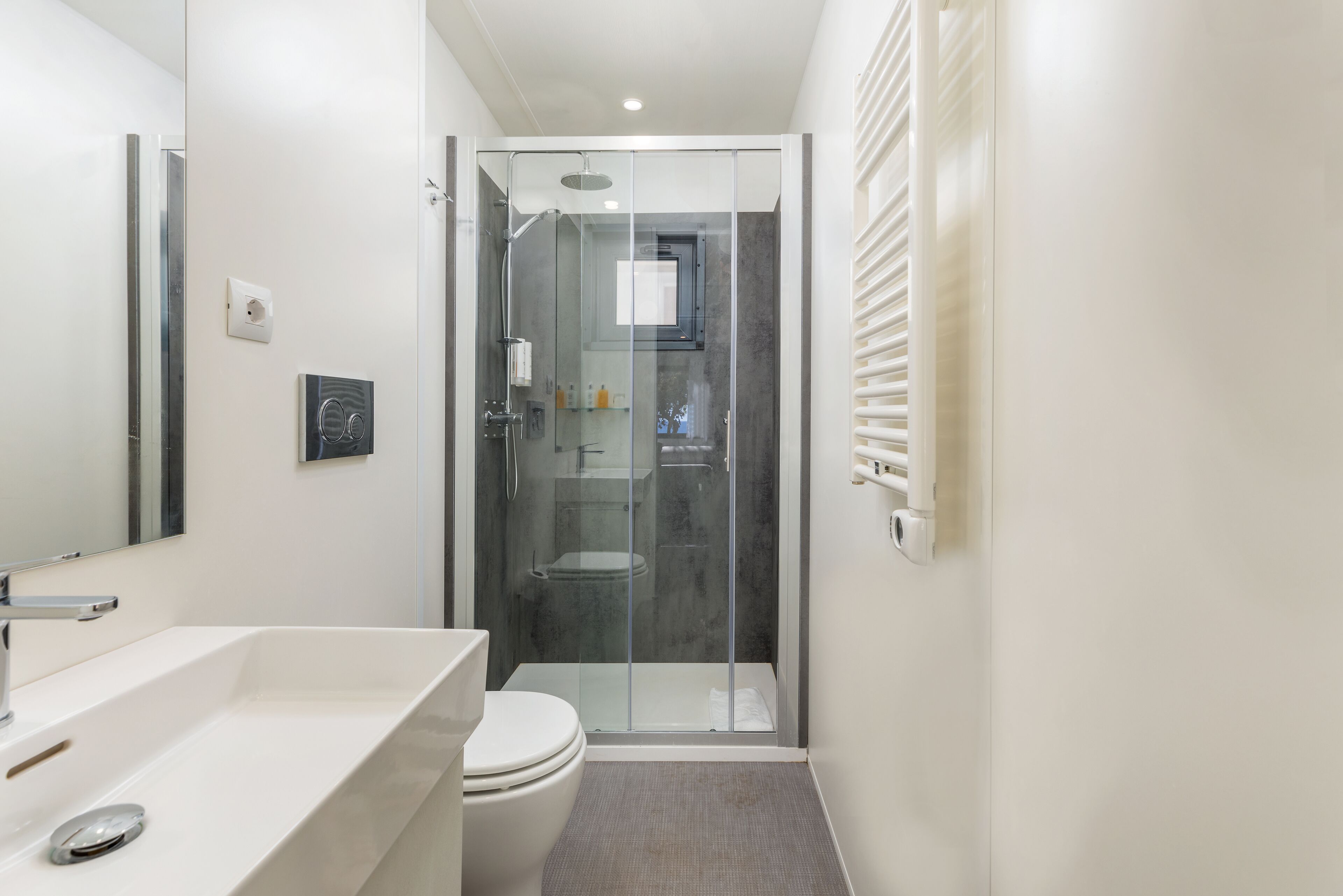 A modern bathroom with a glass-enclosed shower, a white sink, and a toilet.