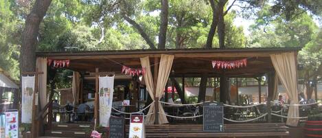 A rustic outdoor seating area with a wooden structure, ropes, and banners.