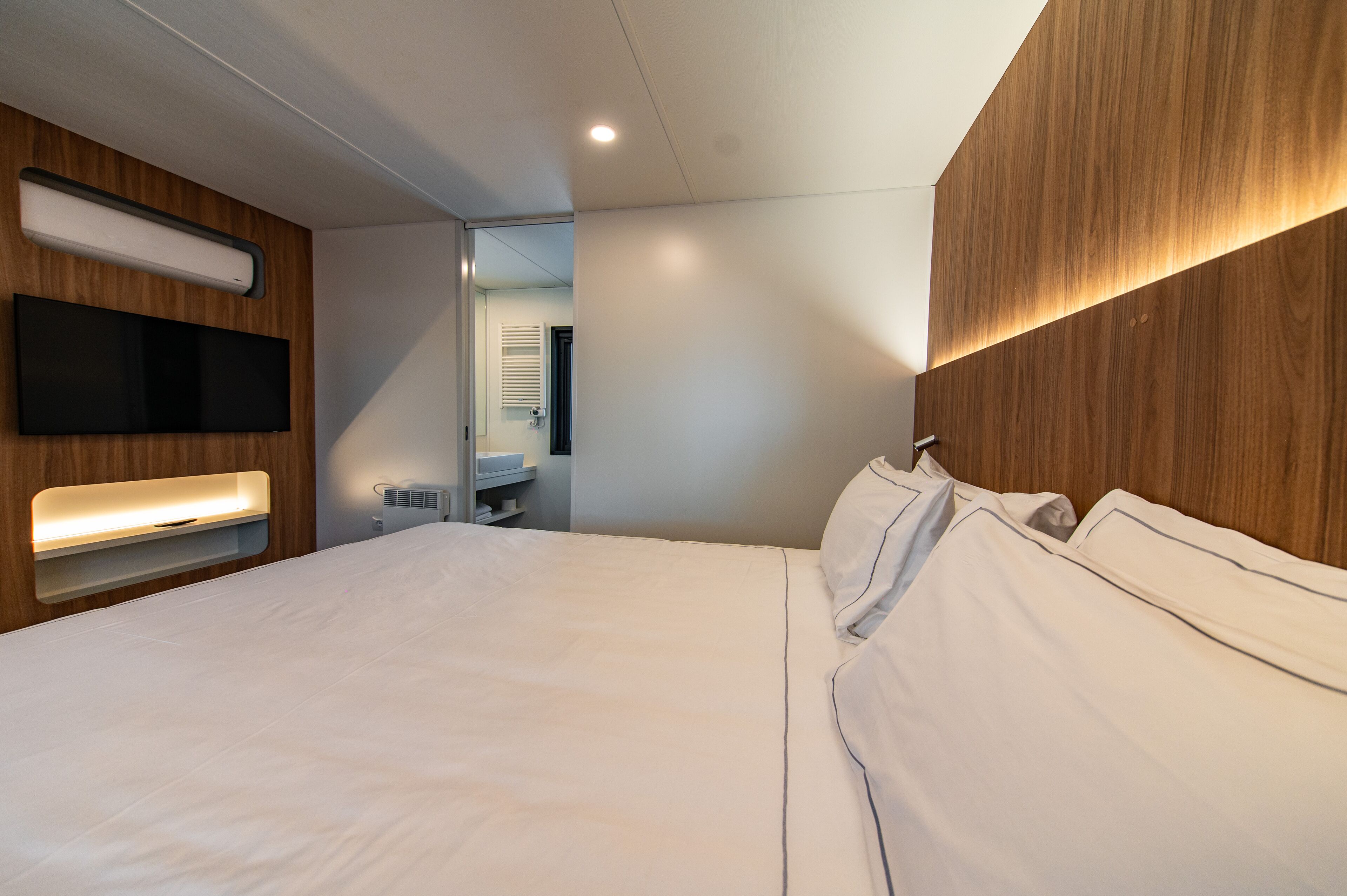 Une chambre d’hôtel moderne dotée d’un grand lit, d’un téléviseur intégré et d’un mur décoratif en bois.