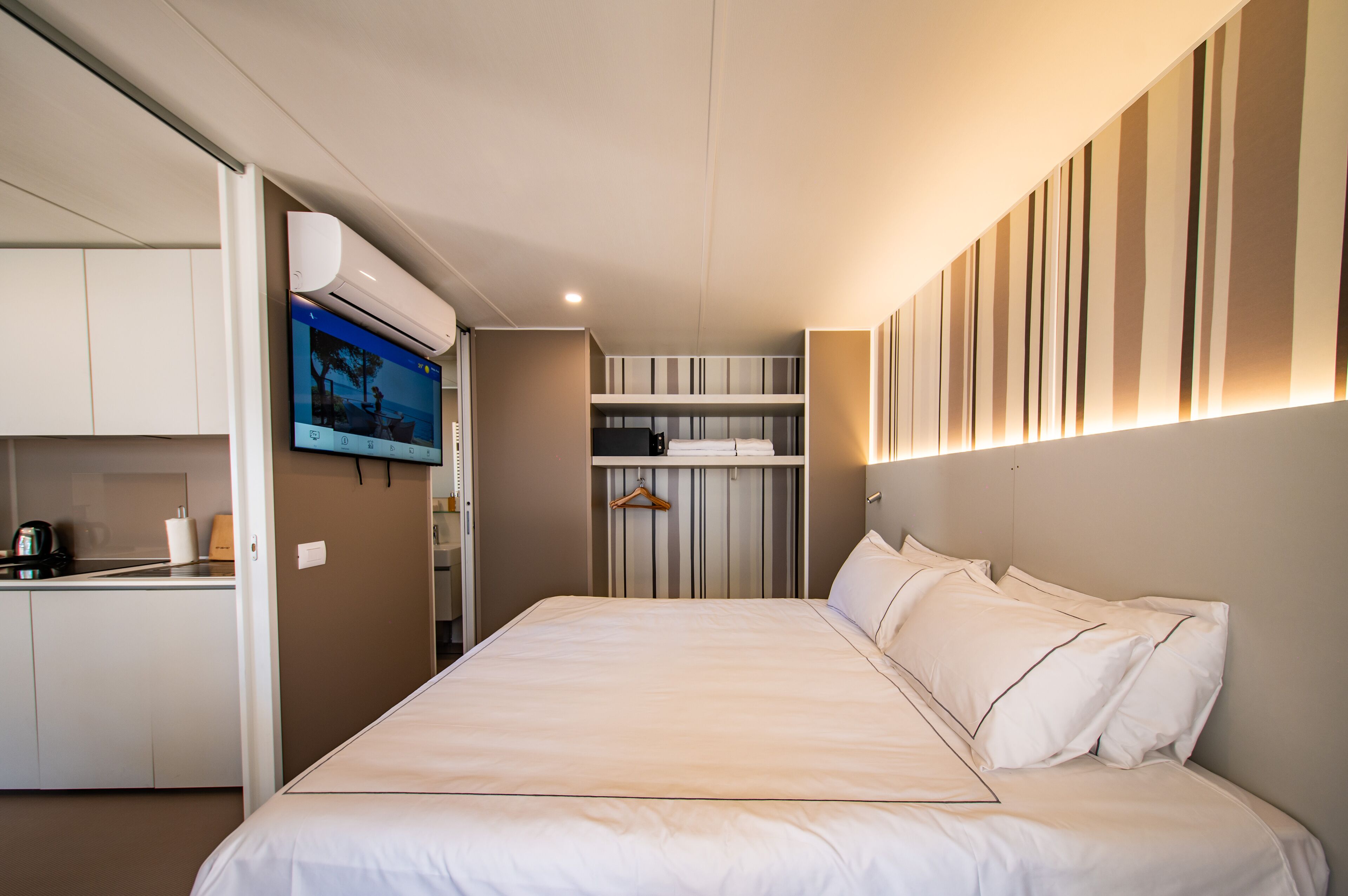 Een hotelkamer met een bed, een aan de muur bevestigde televisie, een kitchenette en een garderobe.