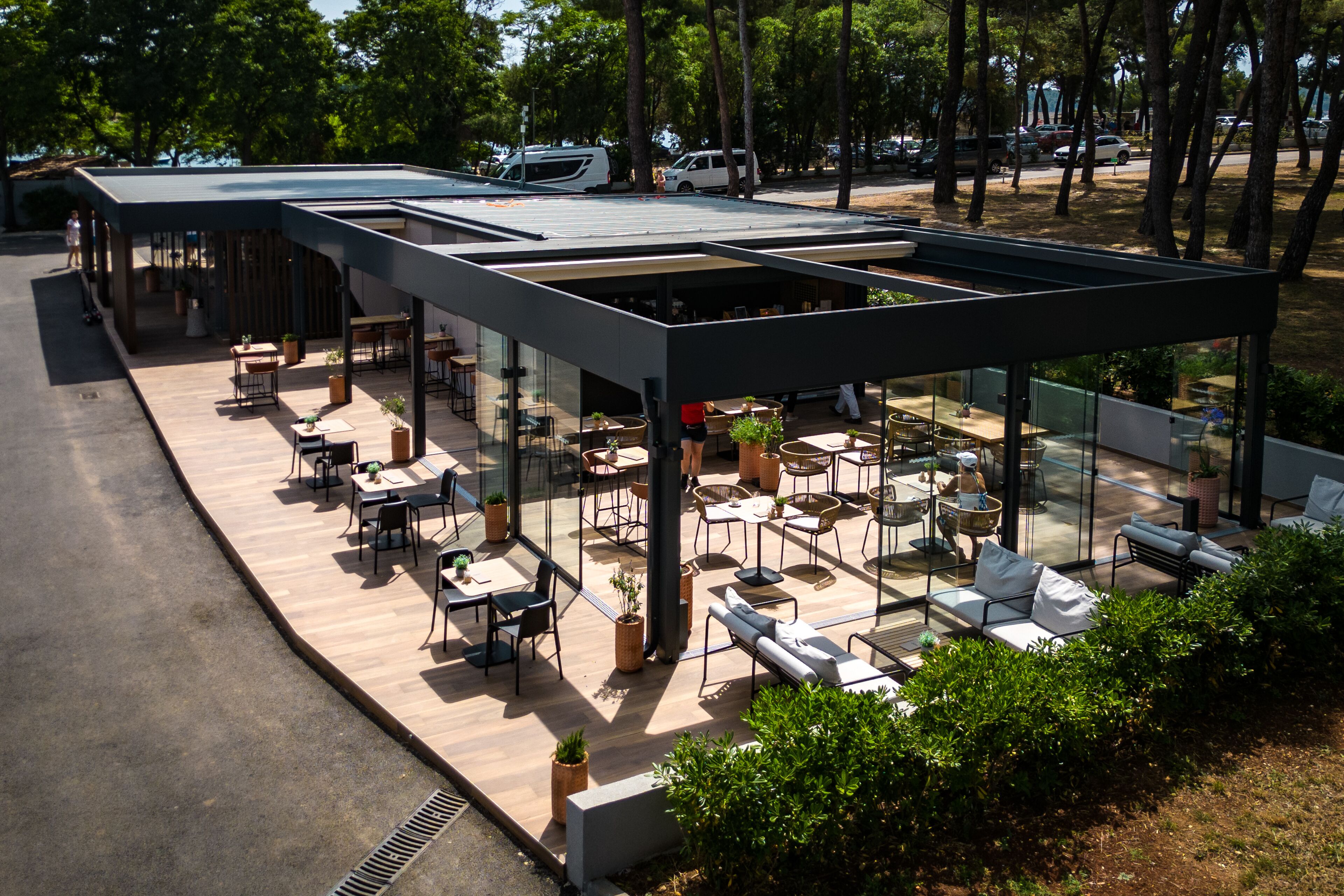 Un espace extérieur aménagé en terrasse, avec plusieurs tables et chaises, entouré de murs de verre et de plantes en pot.