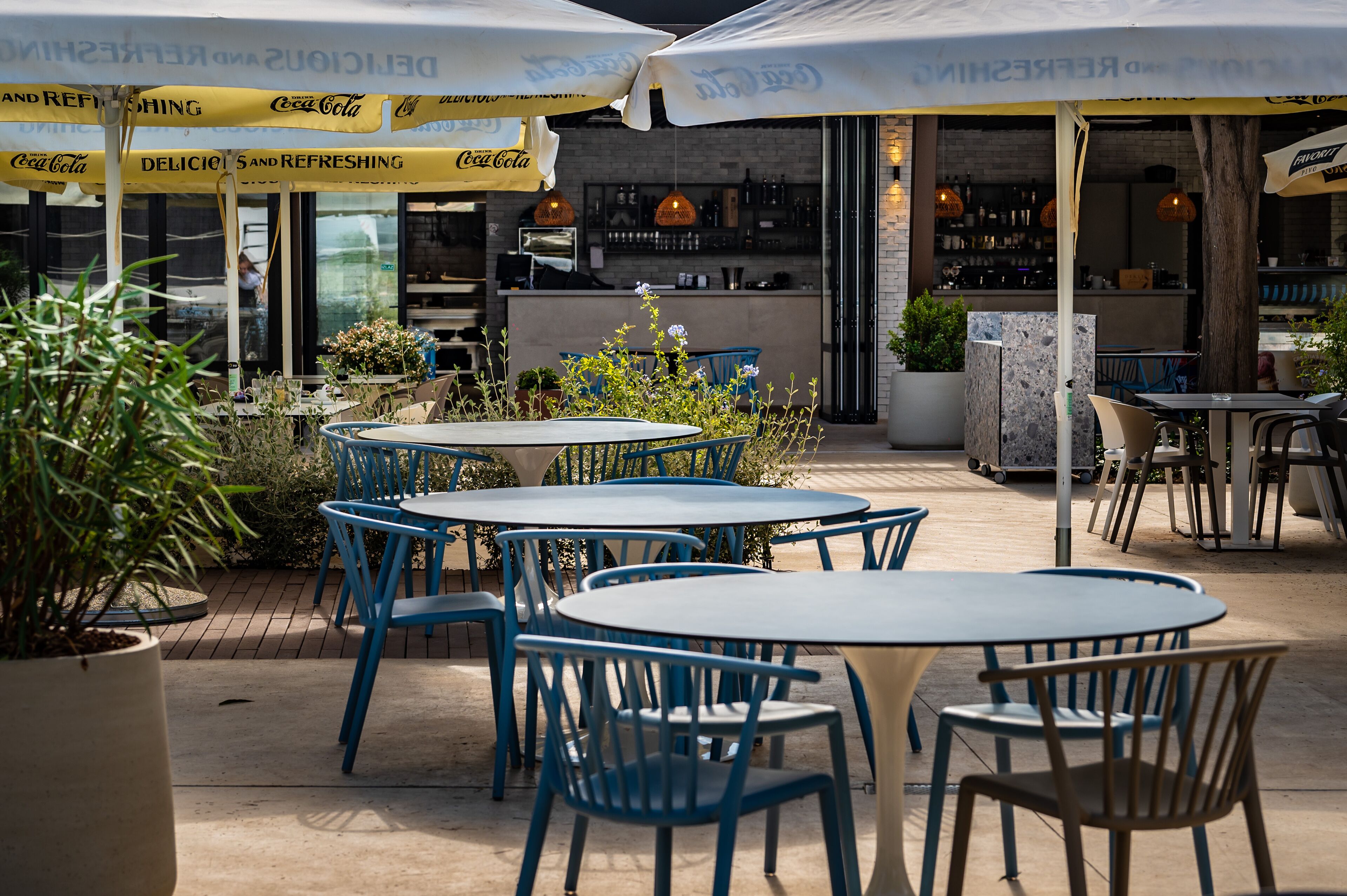 Un espace extérieur aménagé avec des tables et des chaises rondes, des parasols et des plantes en pot.
