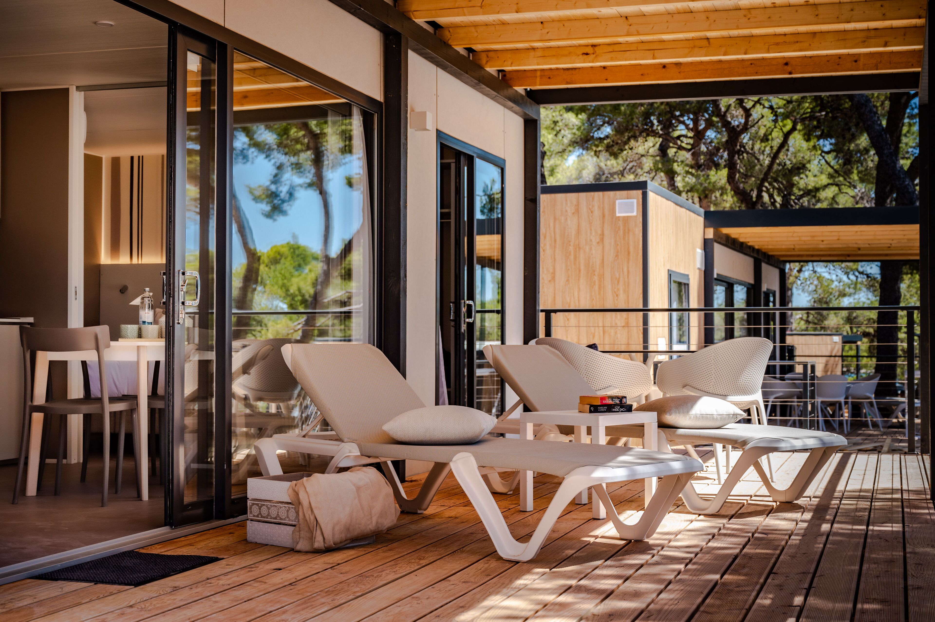 A modern outdoor lounge area with white lounge chairs and a wooden deck.