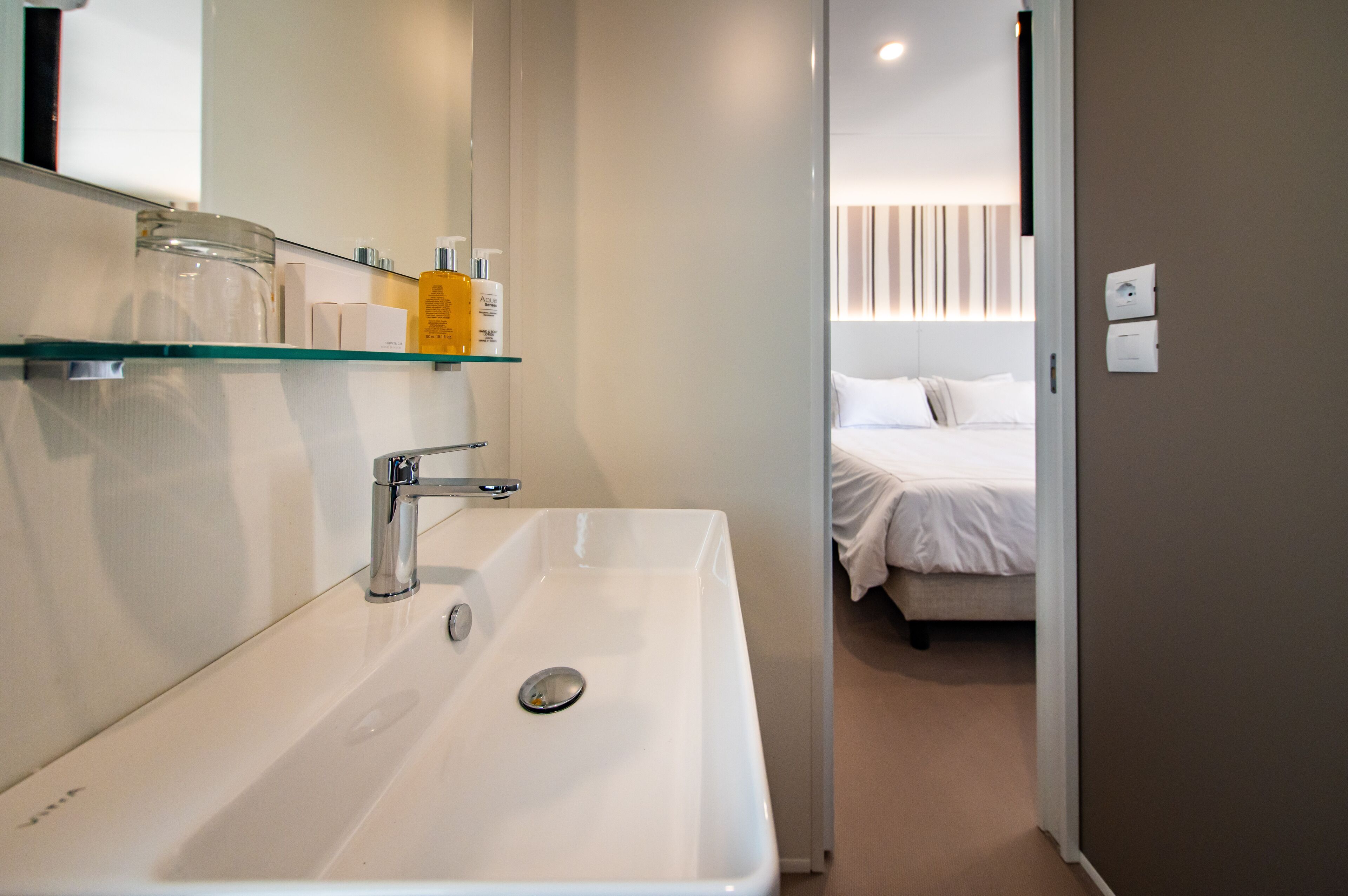 A modern bathroom with a white sink, glass shelf, and toiletries.