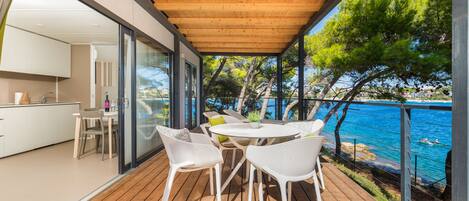 A wooden deck with a table and chairs, overlooking a body of water and trees.
