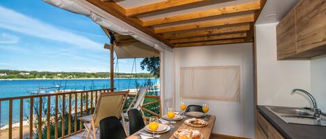 A dining area with a view of the sea, wooden beams, a table set for two, and a small kitchen area.