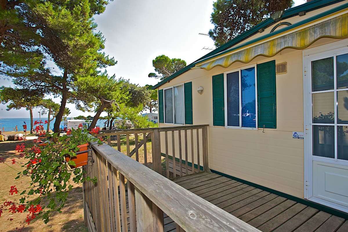 A coastal building with a wooden deck, green shutters, and a view of the sea.