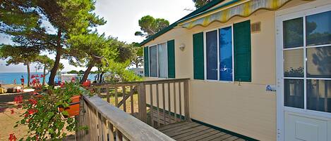 A coastal building with a wooden deck, green shutters, and a view of the sea.