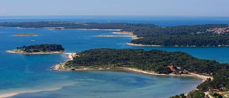 An aerial view of a coastal area with multiple islands, clear blue waters, and a densely forested peninsula.