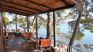 Un espace extérieur abrité, avec des tables et des chaises en bois, offrant une vue sur un plan d’eau et des arbres.