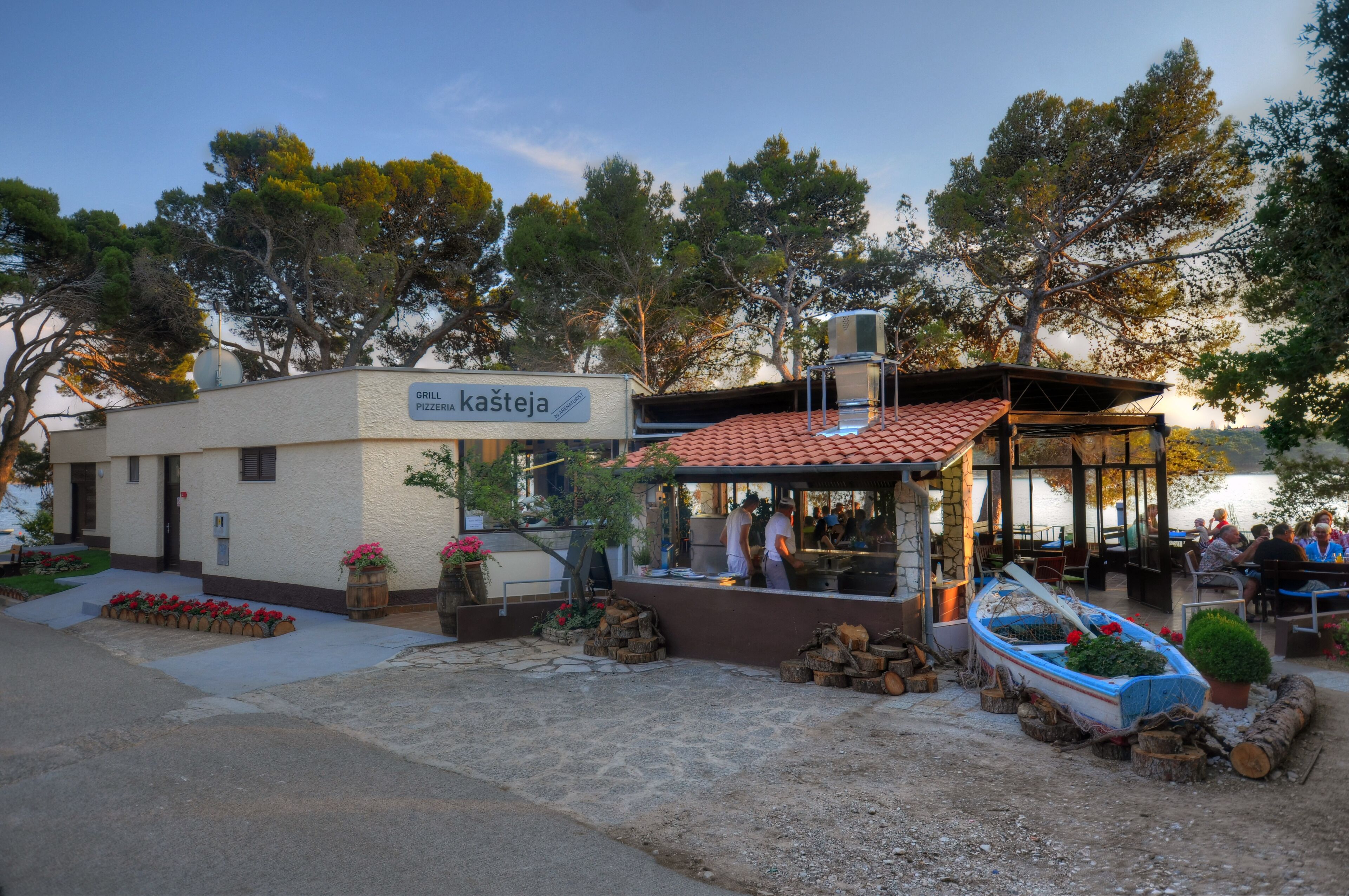 A restaurant with outdoor seating, a sign reading "GRILL kašteja," and a boat near the entrance.