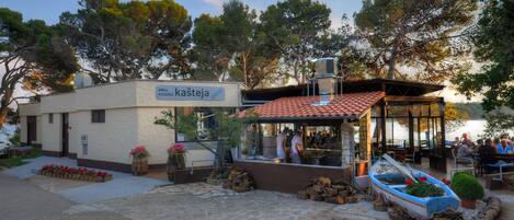 A restaurant with outdoor seating, a sign reading "GRILL kašteja," and a boat near the entrance.