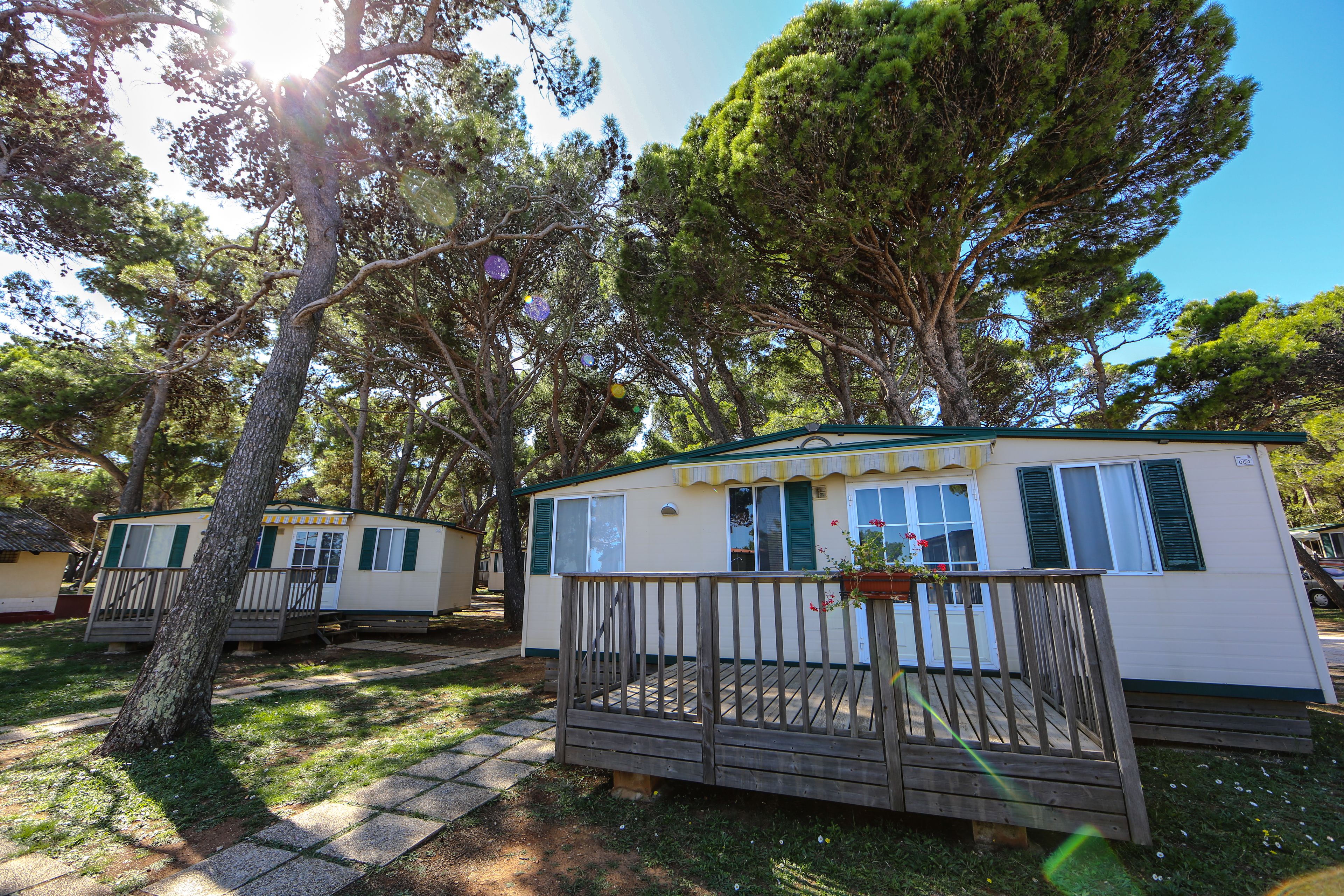 A row of mobile homes with wooden decks and green shutters, surrounded by trees.