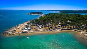 An aerial view of a coastal area with a beach, a small island, and a dense cluster of trees and buildings. - Arena Medulin Mobile Homes (Medulin)
