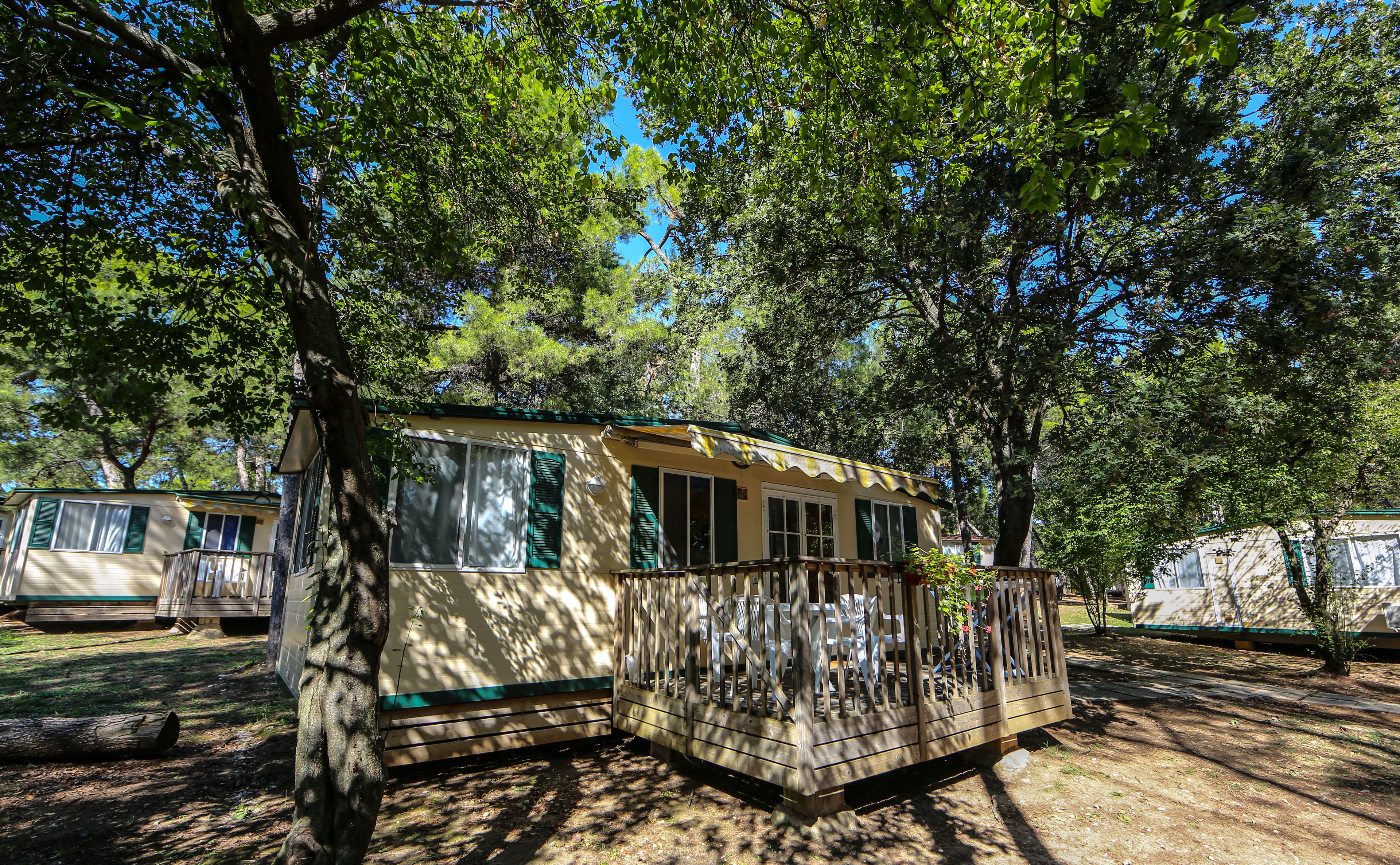A mobile home with a fenced porch, surrounded by trees.