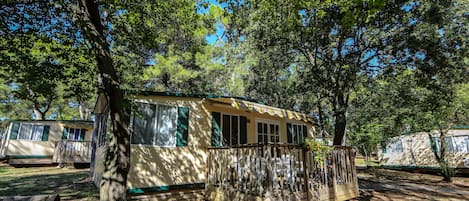 A mobile home with a fenced porch, surrounded by trees.