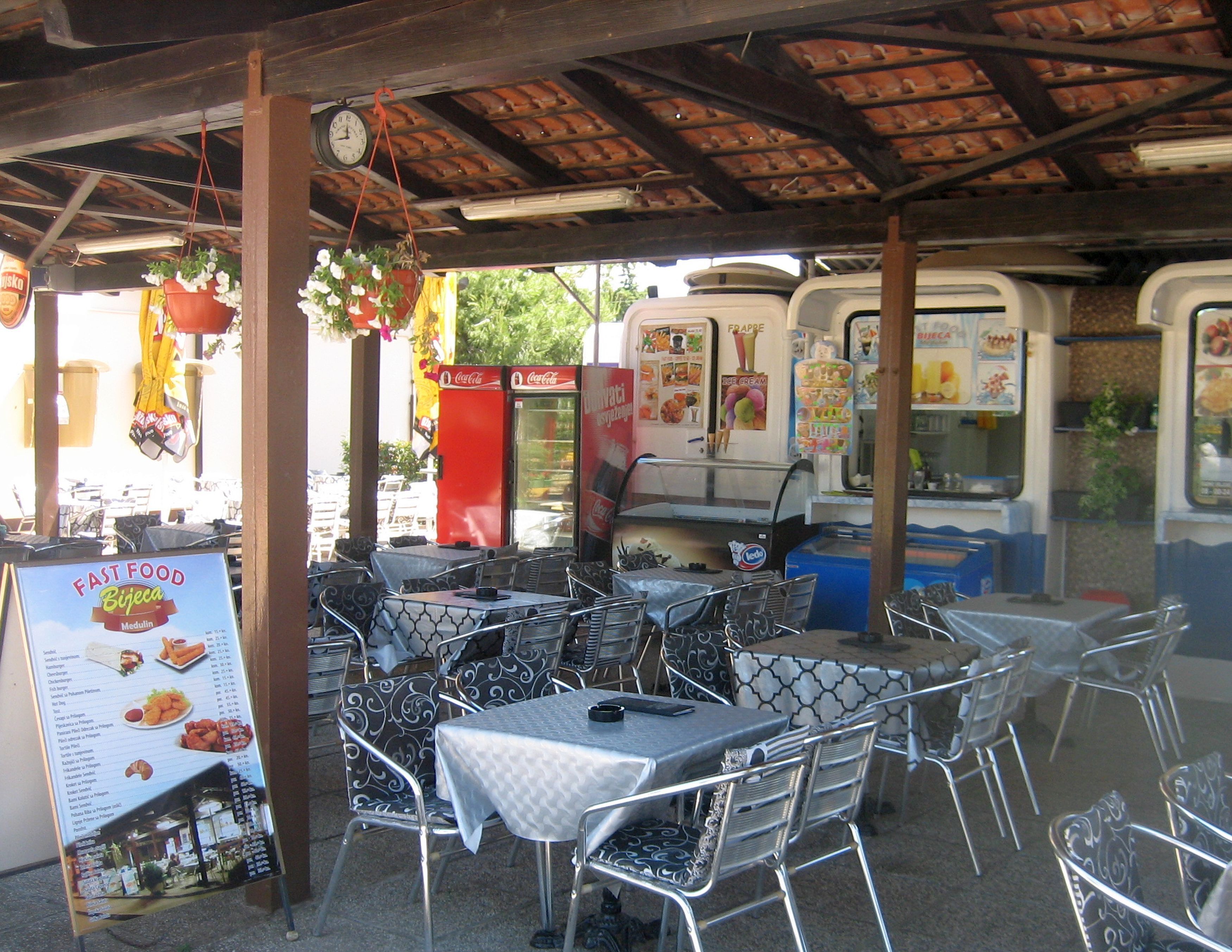 A fast food restaurant with outdoor seating, a Coca-Cola vending machine, and a menu board.