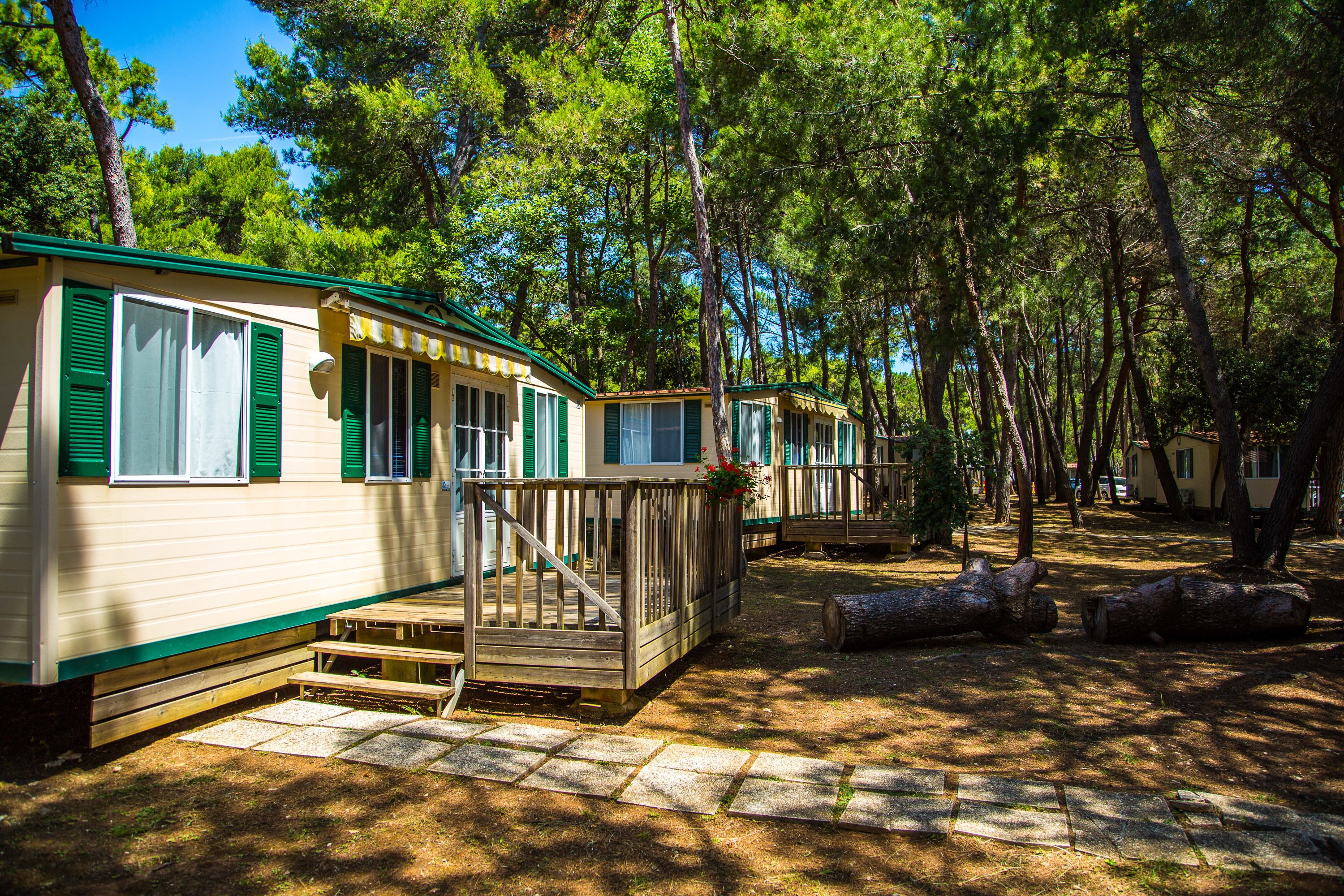 Una hilera de casas móviles con persianas verdes, terrazas de madera y un camino de piedra.