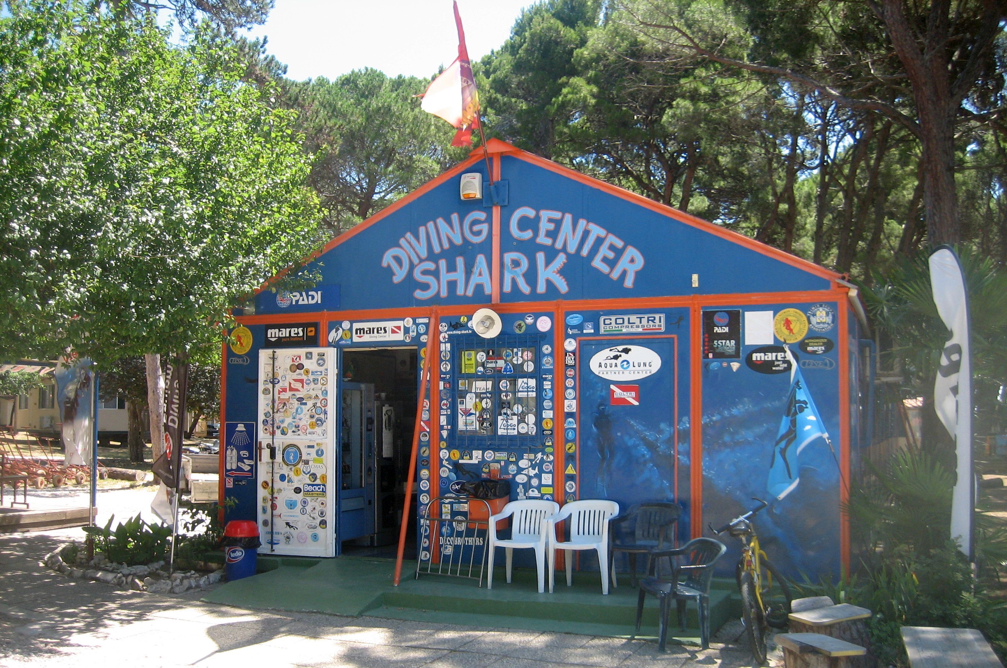 A small, colorful building with a sign reading "Diving Center Shark," surrounded by trees.