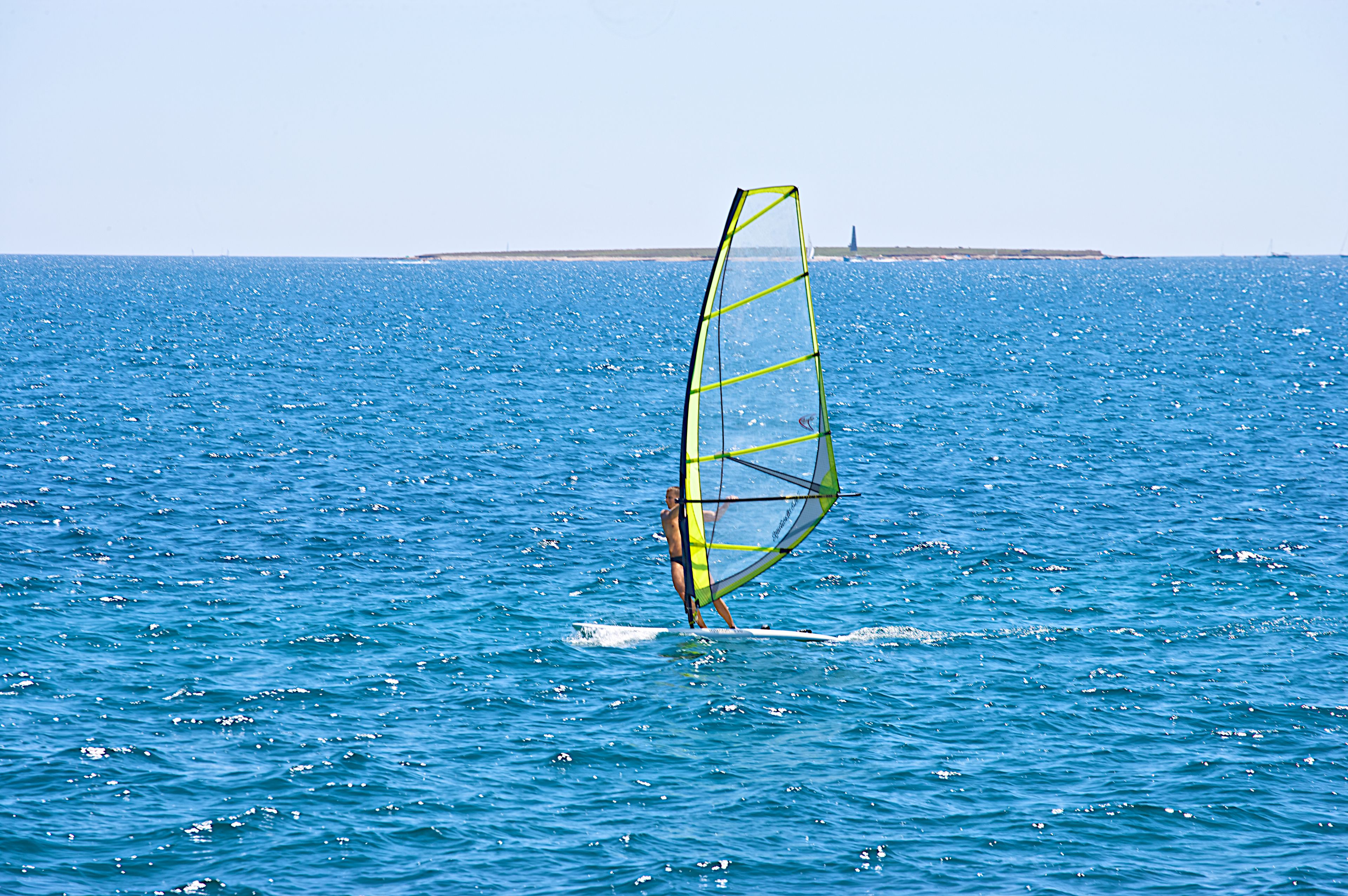 Eine Person windsurft auf einem großen Gewässer bei blauem Himmel.