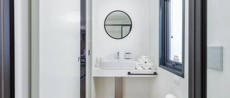 A modern bathroom with a white sink, a round mirror, and a window.
