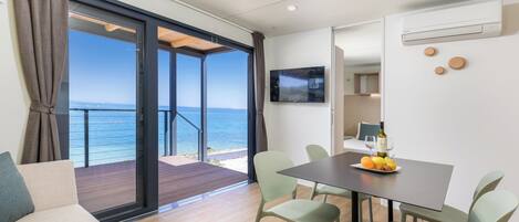 A modern room with a dining table, chairs, a TV, and a view of the sea.