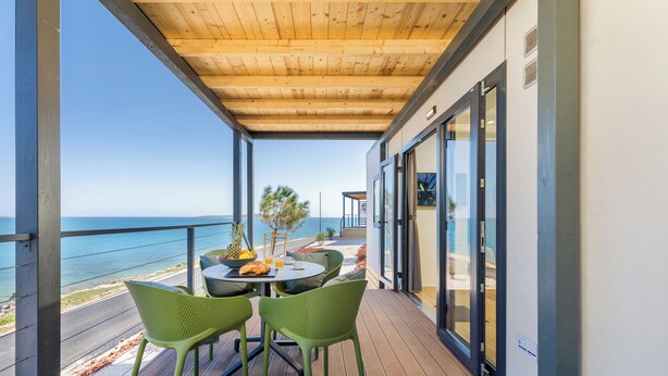 A balcony with a wooden ceiling, a table with chairs, and a view of the sea. - Arena Stupice Camping Homes (Medulin)