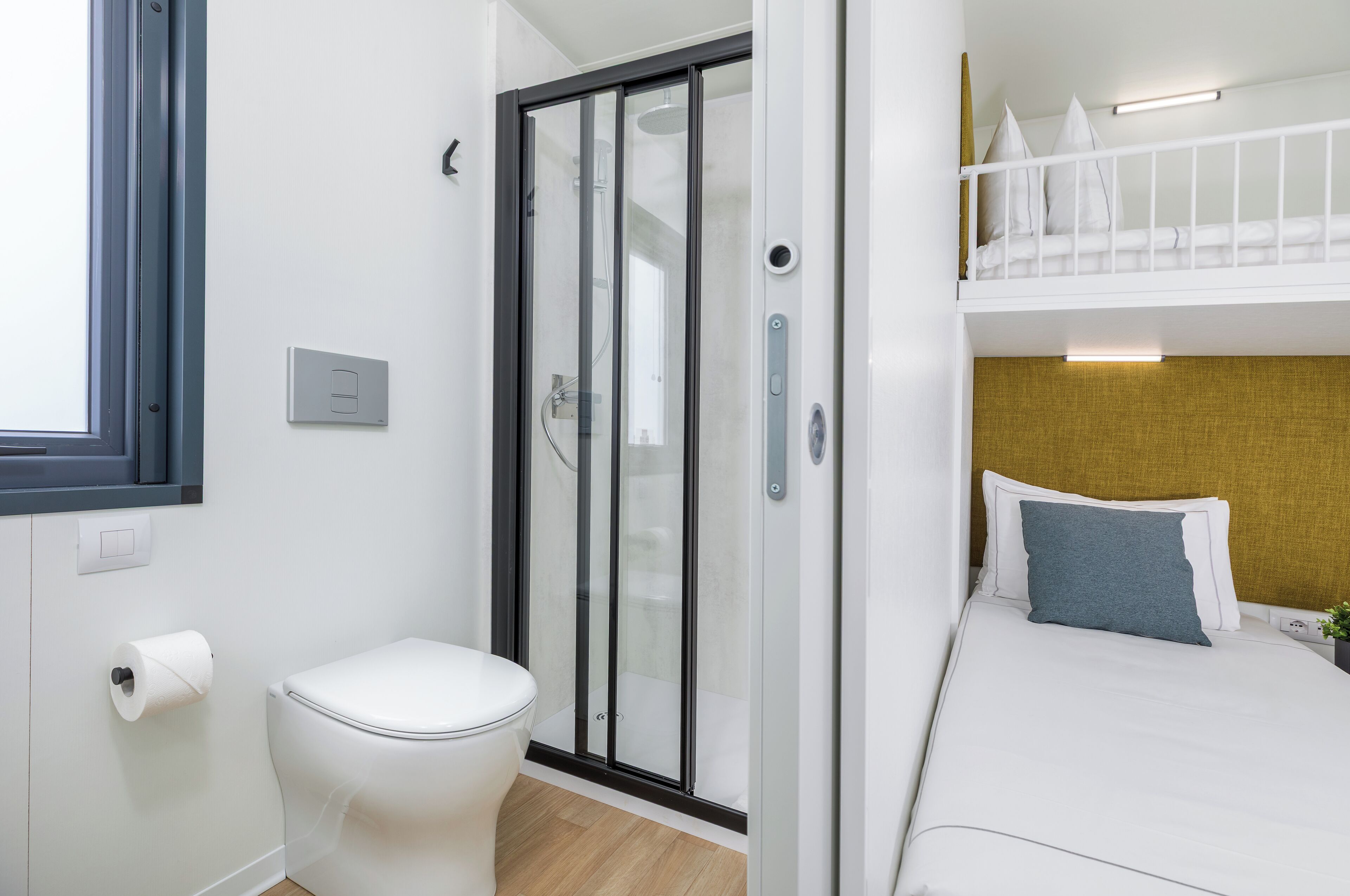 Camera d'albergo compatta con doccia, WC e letto a castello.