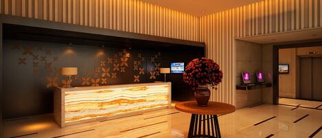 A modern reception area with a marble reception desk, a vase with red flowers, and a digital screen displaying information.