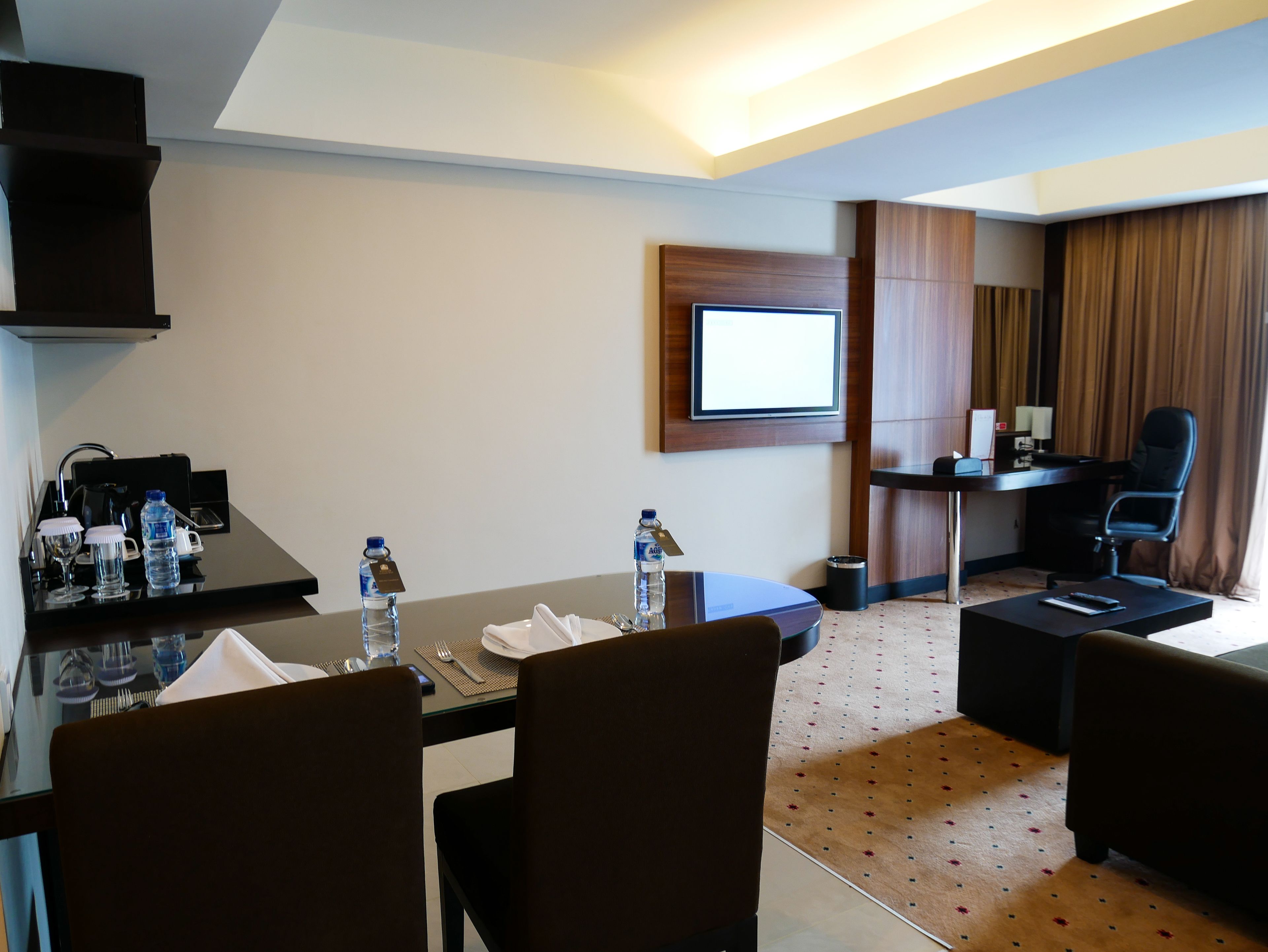 Una camera d'albergo con un tavolo da pranzo per quattro persone, una TV montata a parete, una scrivania con una sedia e un letto con tende.