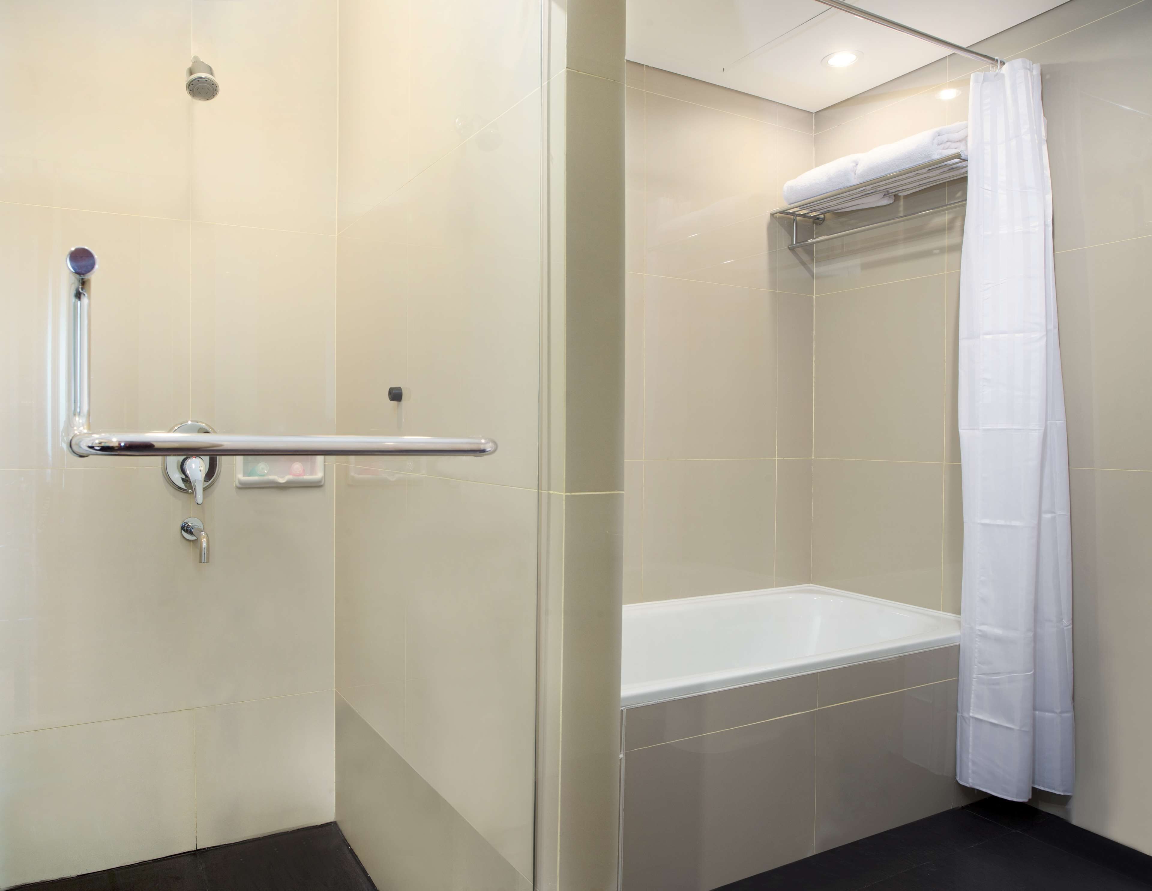 A modern bathroom with a glass shower enclosure, a white bathtub, and a handrail.
