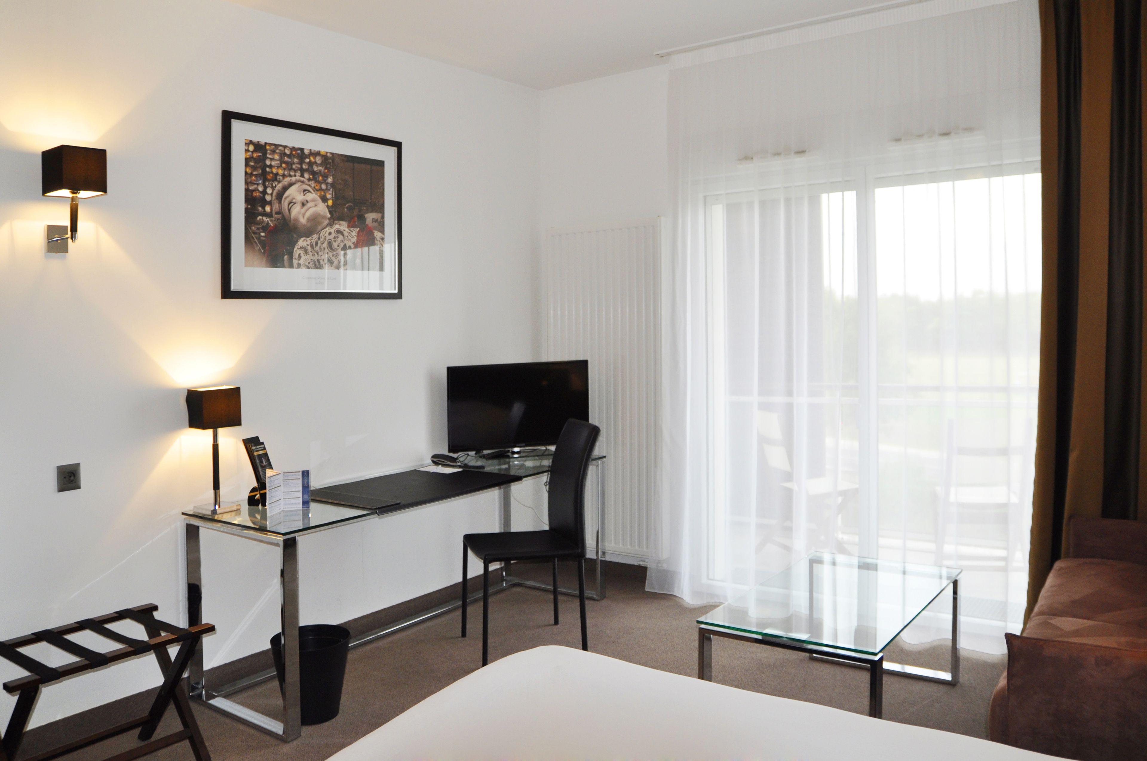 Une chambre d’hôtel avec un lit, un bureau avec un ordinateur, une chaise, une télévision et une fenêtre avec des rideaux.