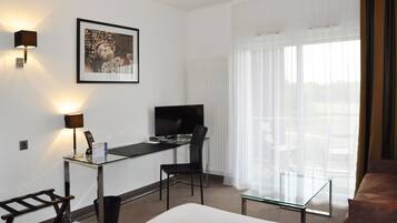 Une chambre d’hôtel avec un lit, un bureau avec un ordinateur, une chaise, une télévision et une fenêtre avec des rideaux.