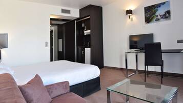 Una habitación de hotel moderna con cama, una mesa de centro de vidrio, un escritorio con silla, televisor y un cuadro en la pared.