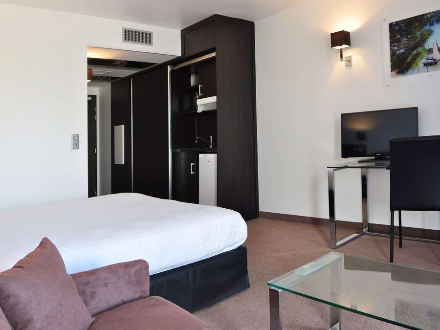 A modern hotel room with a bed, a glass coffee table, a desk with a chair, a TV, and a painting on the wall.