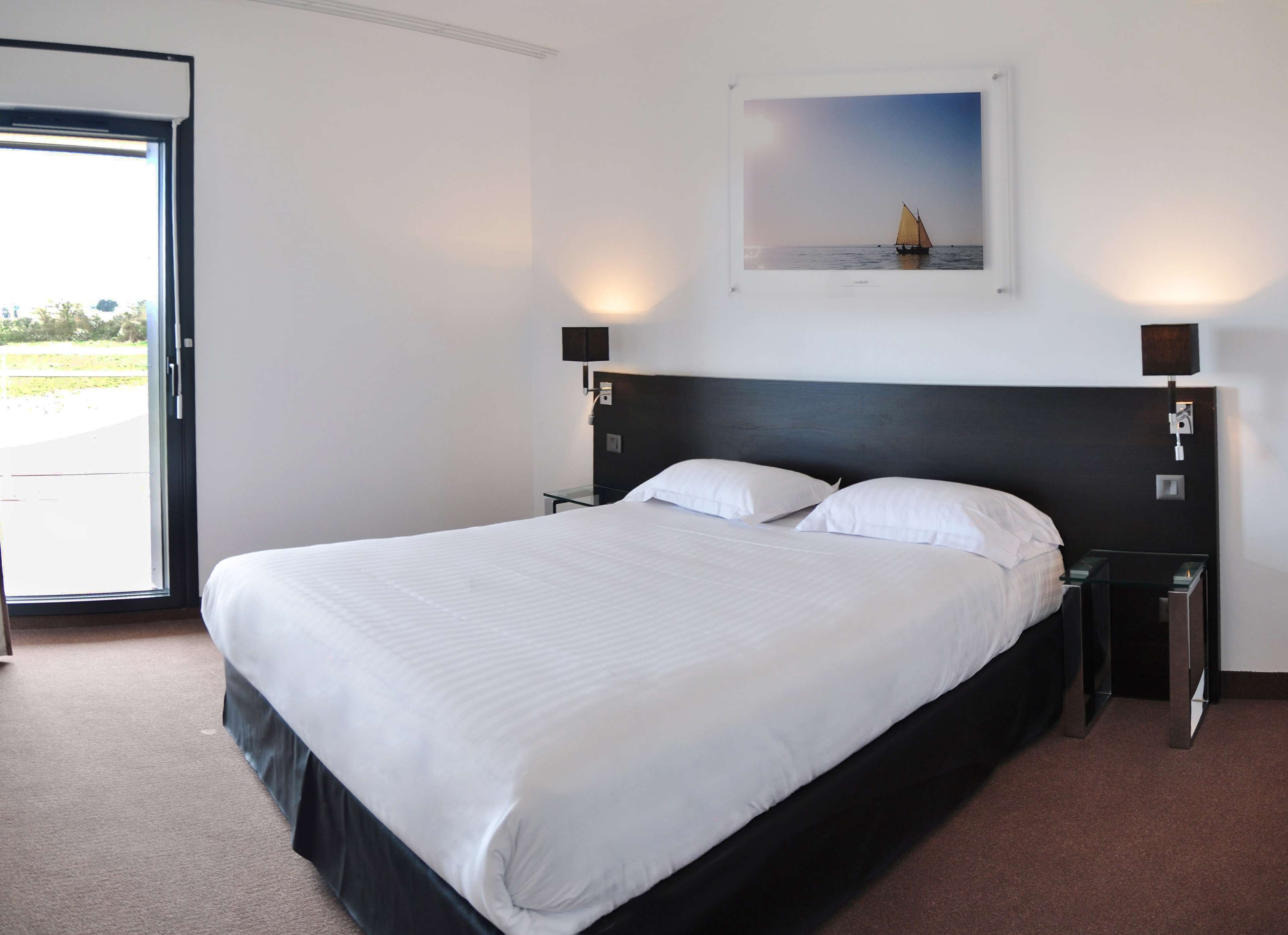 A hotel room with a large bed, two bedside tables, a door leading to a balcony, and a framed picture on the wall.