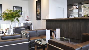 Um lobby de hotel moderno com assentos de couro, área de bar com prateleiras de garrafas e obras de arte nas paredes.