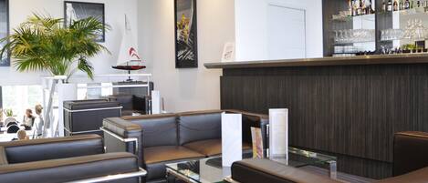 A modern hotel lobby with leather seating, a bar area with shelves of bottles, and artwork on the walls.