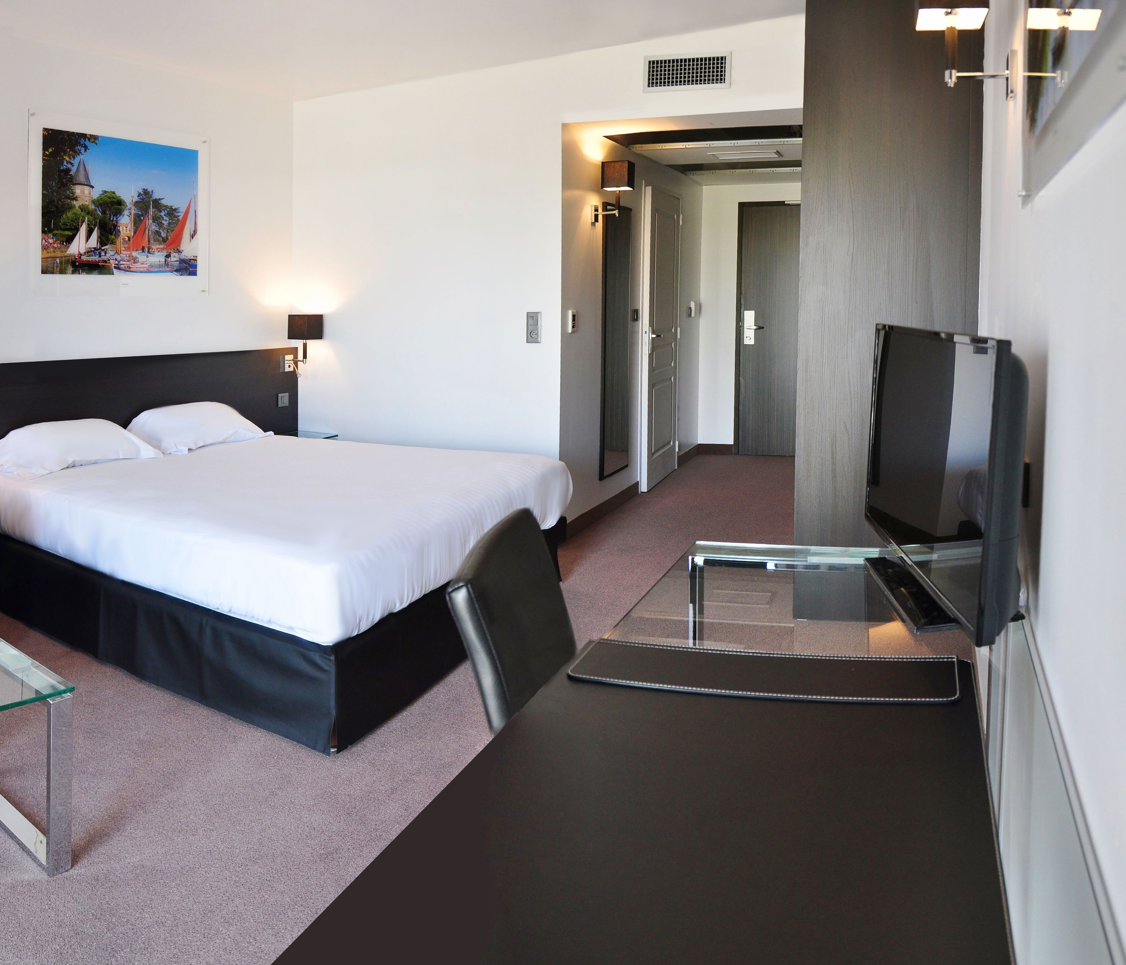 Een hotelkamer met een bed, een televisie, een glazen tafel en een schilderij aan de muur.