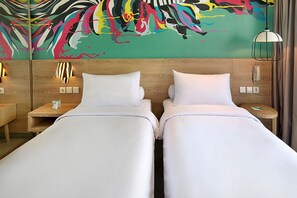 A hotel room with two beds, a colorful abstract mural on the wall, wooden headboards, bedside tables with lamps, and a modern pendant light.